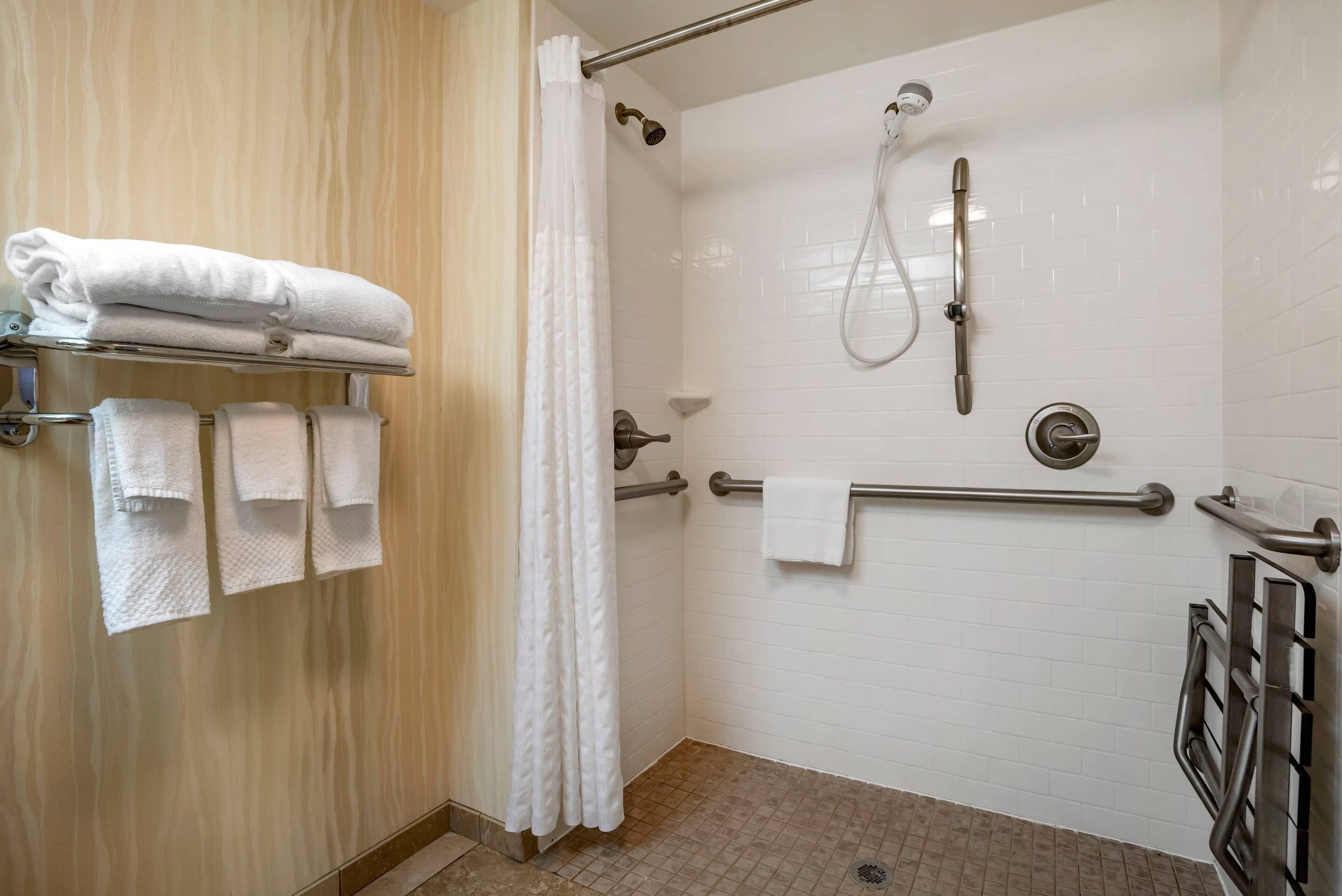 A shower area with a handheld showerhead, a grab bar, and a towel rack with folded towels.