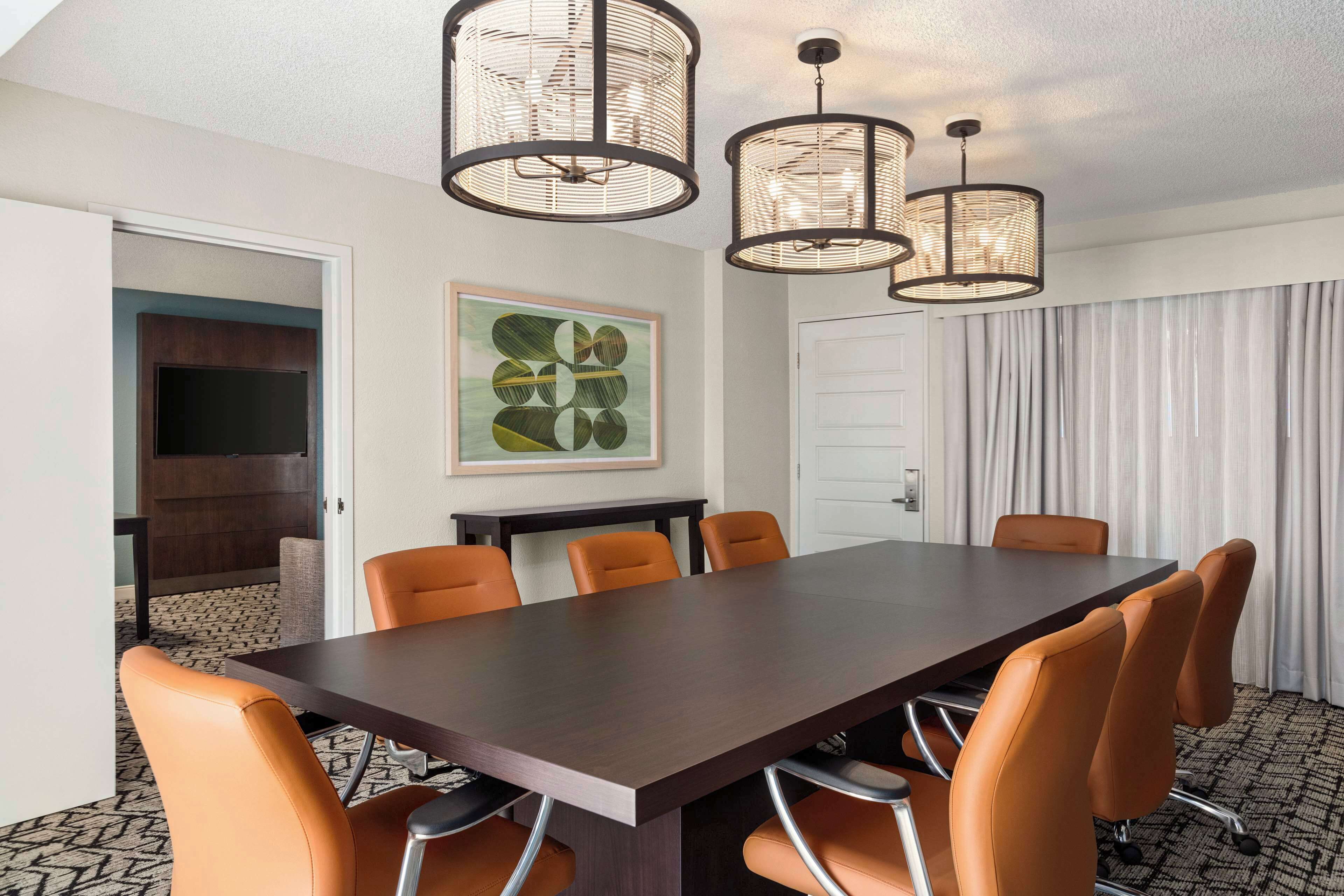 Une salle de conférence avec une grande table en bois foncé, des chaises orange et trois luminaires suspendus.
