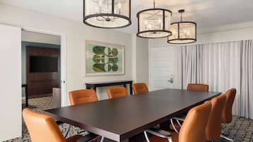 Une salle de conférence avec une grande table en bois foncé, des chaises orange et trois luminaires suspendus.