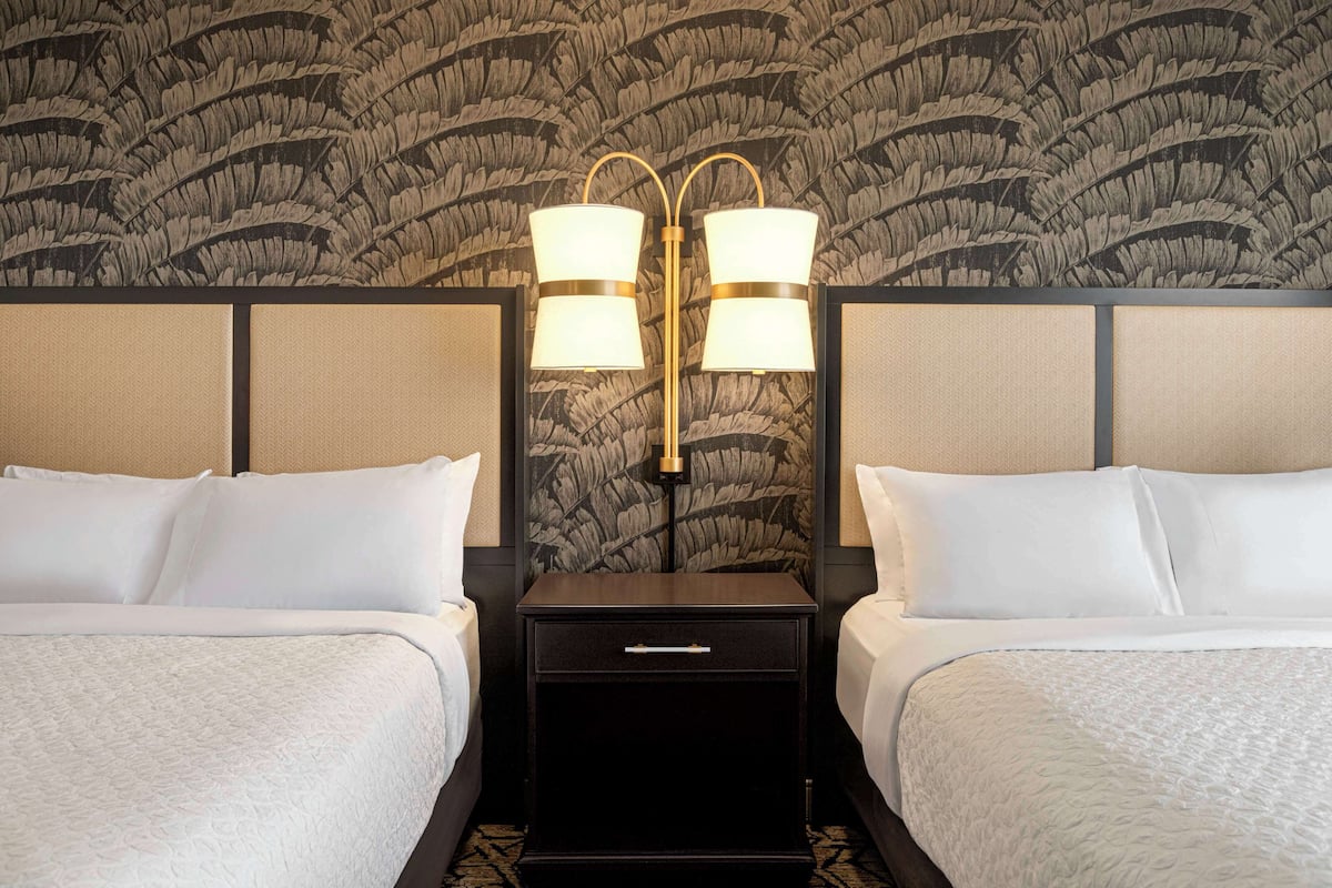 Ein Hotelzimmer mit zwei Betten, einem Nachttisch mit Lampe und einem Wandpapier mit Muster.