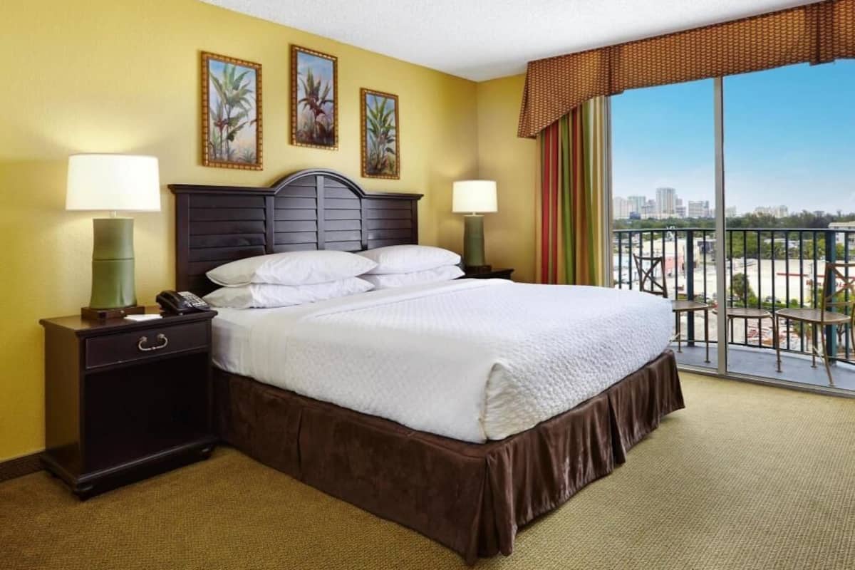 A hotel room with a bed, bedside lamps, a nightstand, and a balcony with a city view.