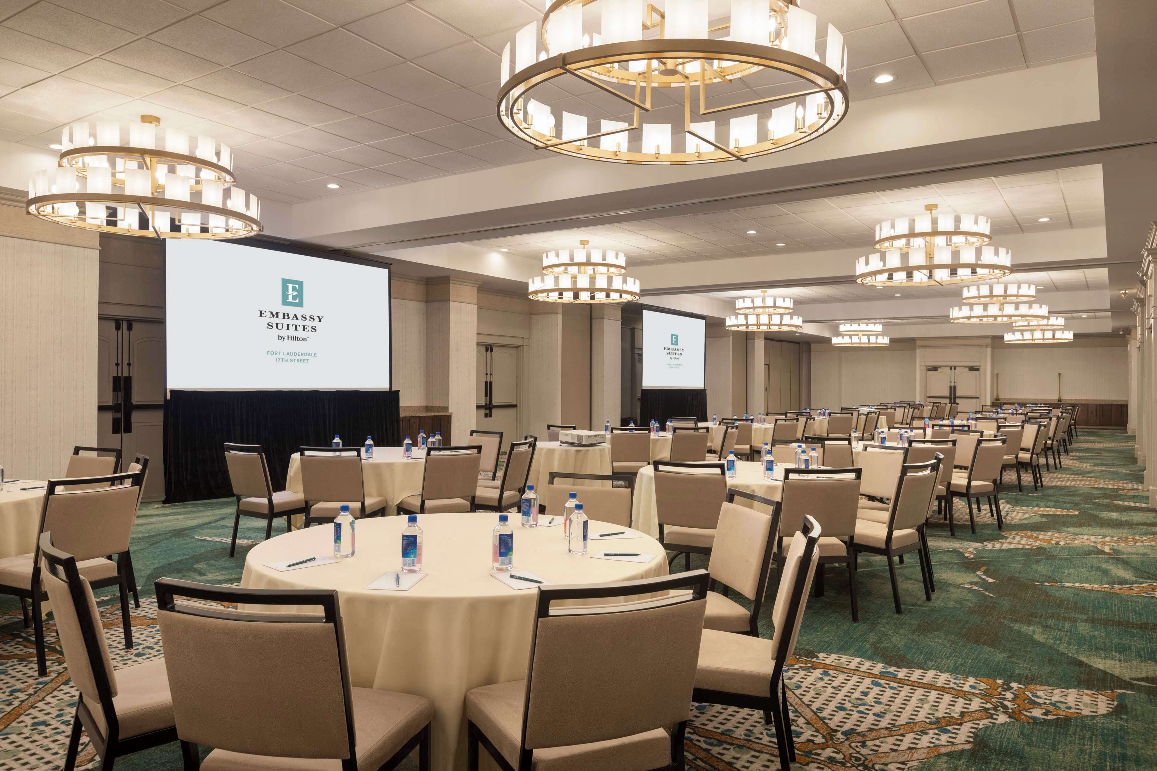 A conference room with round tables, chairs, and a large screen displaying the Embassy Suites logo.