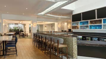 A modern bar area with a long counter, bar stools, and a display of liquor bottles.