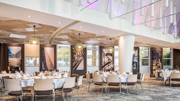 A spacious dining area with round tables, chairs, and modern lighting fixtures. - Novotel Lyon Gerland (Lyon)