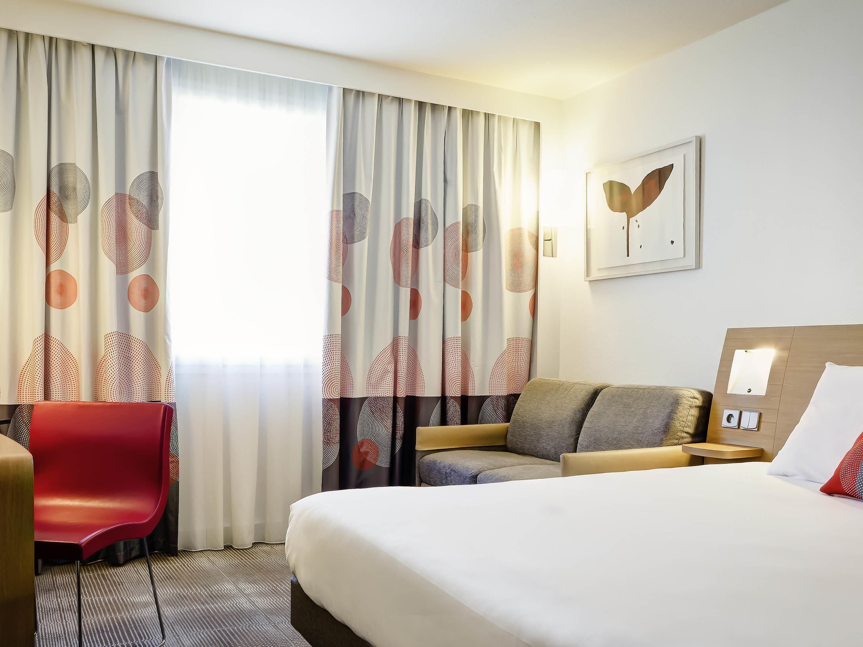 A hotel room with a bed, a sofa, a red chair, and a desk.