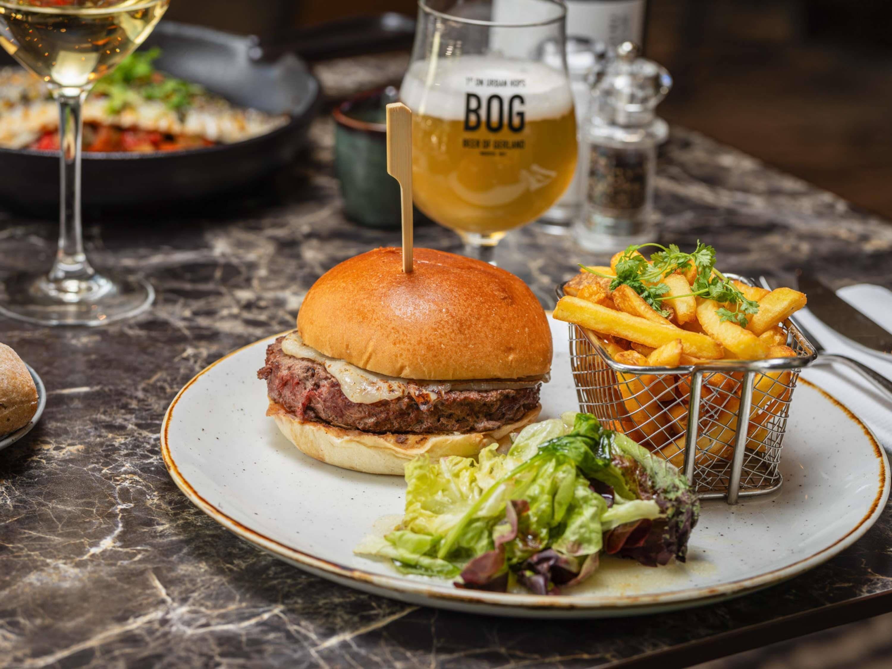 A burger with a bun, a glass of beer, fries, and a side salad on a plate.