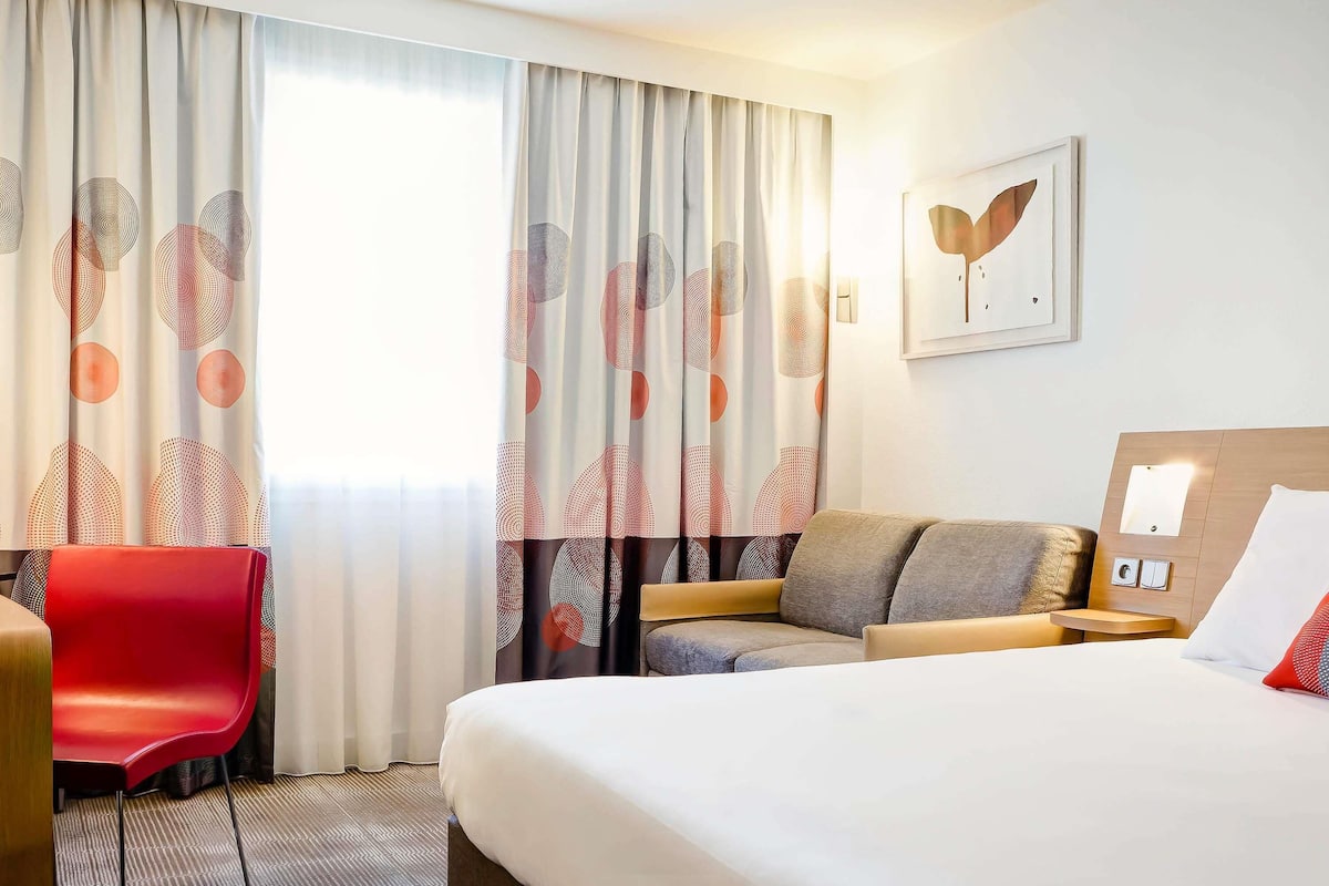 Una habitación de hotel con cama, sofá, una silla roja y escritorio.