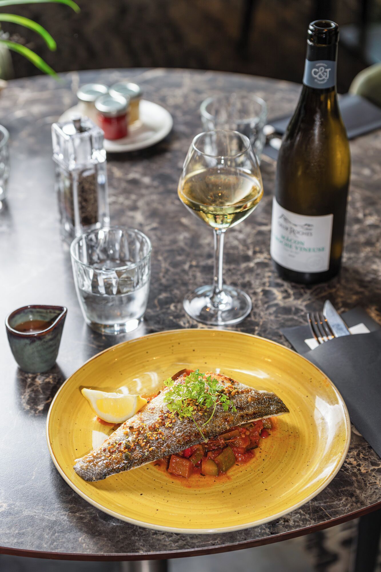 Un tavolo da pranzo con un piatto di pesce, una bottiglia di vino e dei bicchieri.