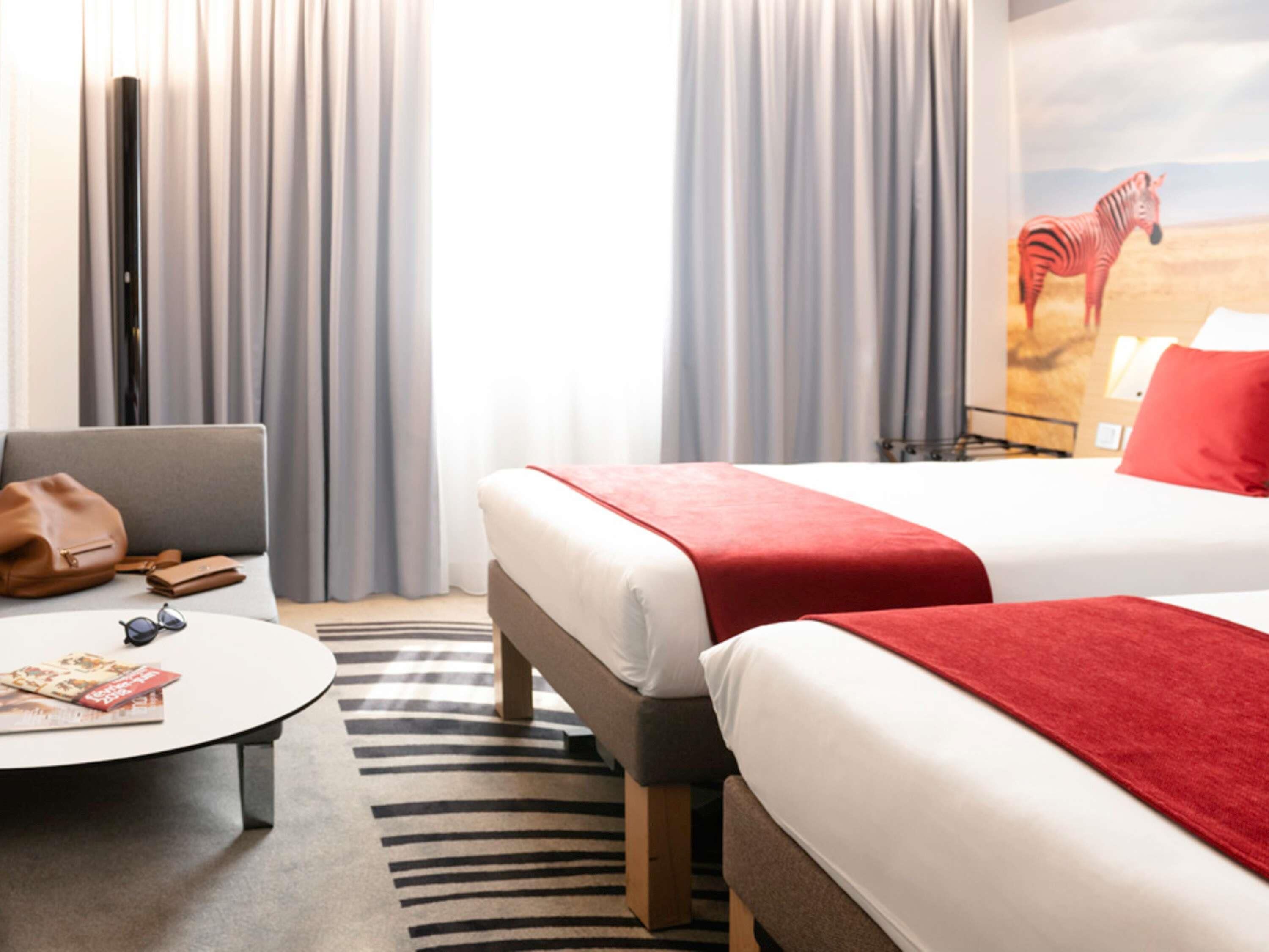 A hotel room with two beds, a sofa, a coffee table, and a zebra mural on the wall.