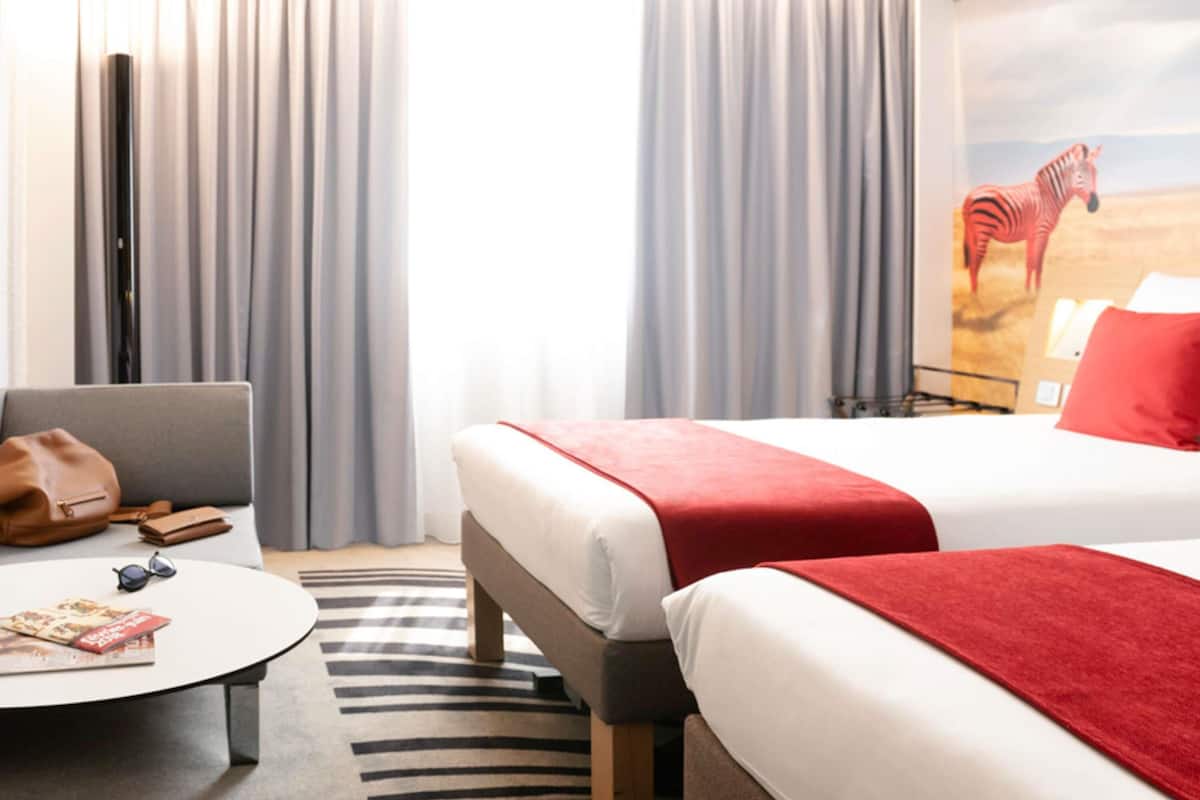 Habitación de hotel con dos camas, un sofá, una mesa de centro y un mural con motivos de cebra en la pared.