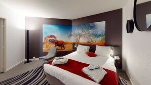 A hotel room with a large bed, a red throw blanket, a white pillow, a red pillow, a nightstand with a phone, and a painting of an elephant and tree on the wall. - Novotel Lyon Gerland (Lyon)
