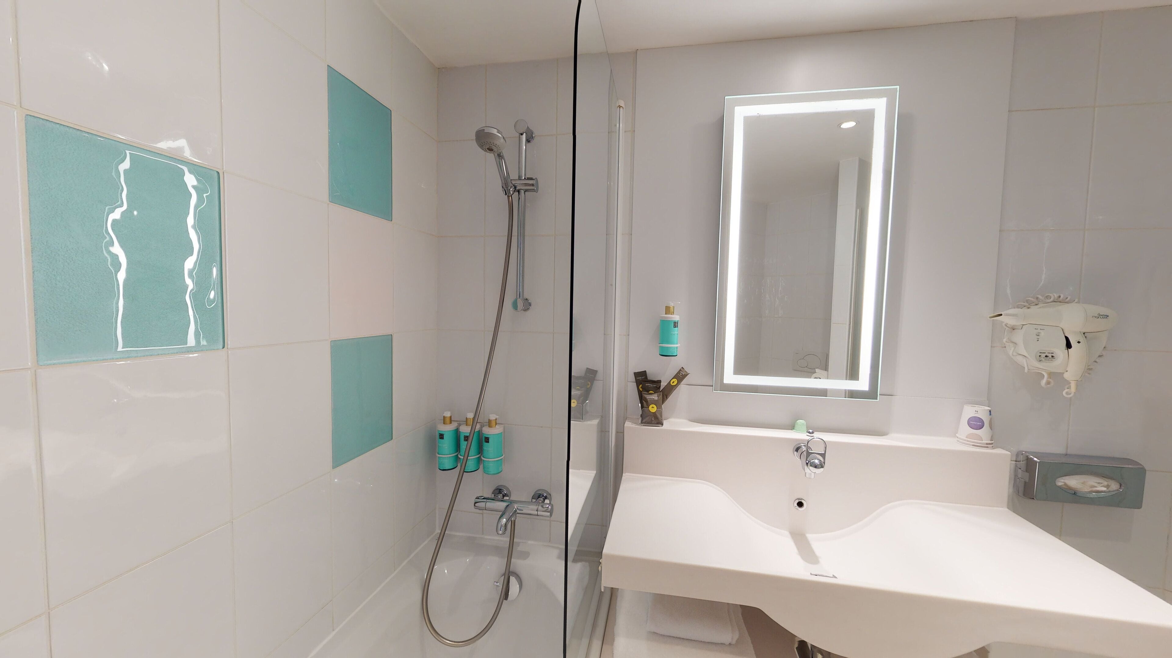 A modern bathroom with a glass-enclosed shower, a white sink, and a mirror with built-in lighting.