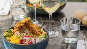 A dining table with a blue bowl containing a salad, two glasses of white wine, and a glass of water.