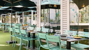 An outdoor dining area with green chairs and tables, umbrellas, and a view of a building with large windows. - Novotel Lyon Gerland (Lyon)