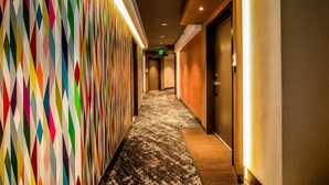 A hallway with a colorful geometric wall pattern, wooden flooring, and a carpeted area leading to a door. - Century Park Hotel (Los Angeles)