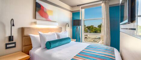 Una habitación de hotel moderna con una cama grande, una mesita de noche, un escritorio y una ventana con vista a la ciudad.