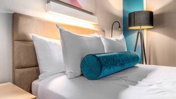A hotel room with a bed, pillows, a nightstand, a lamp, and a painting on the wall.