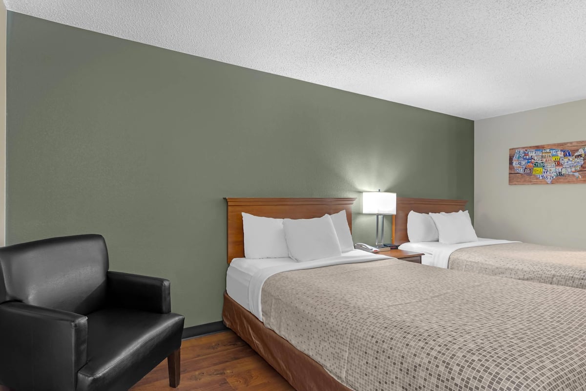 Une chambre d’hôtel avec deux lits, une chaise et une carte géographique accrochée au mur.
