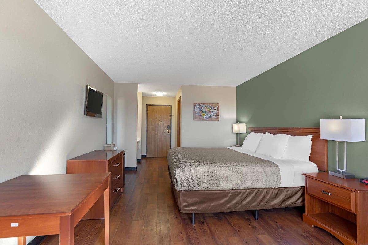 Une chambre d’hôtel comprenant un lit, un bureau, une commode, une télévision, une lampe et une porte donnant sur une autre pièce.