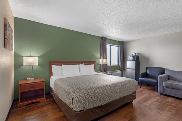 A hotel room with a large bed, a desk, a chair, and a flat-screen TV.