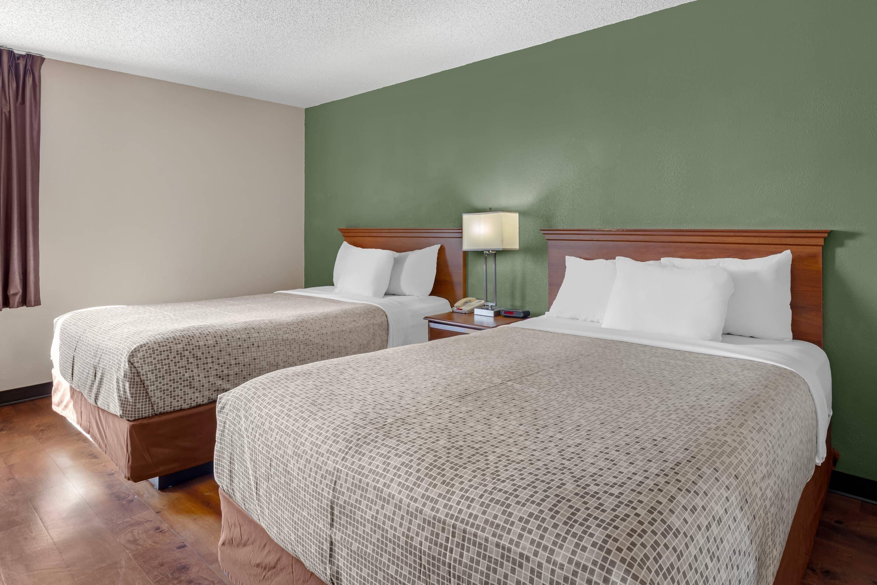 A hotel room with two beds, a nightstand with a lamp, and a green wall.