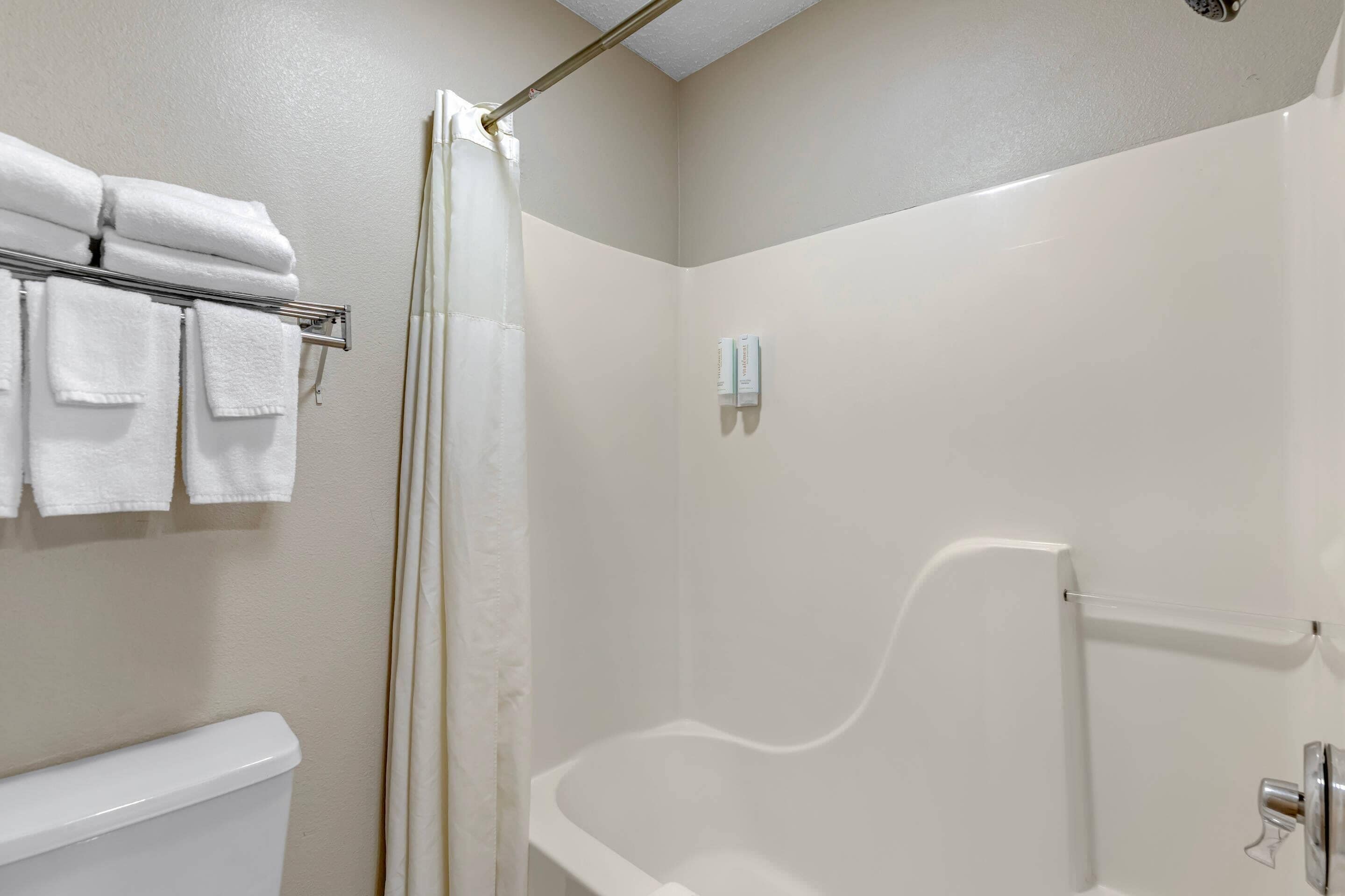 A bathroom with a shower, a toilet, and a towel rack with folded towels.