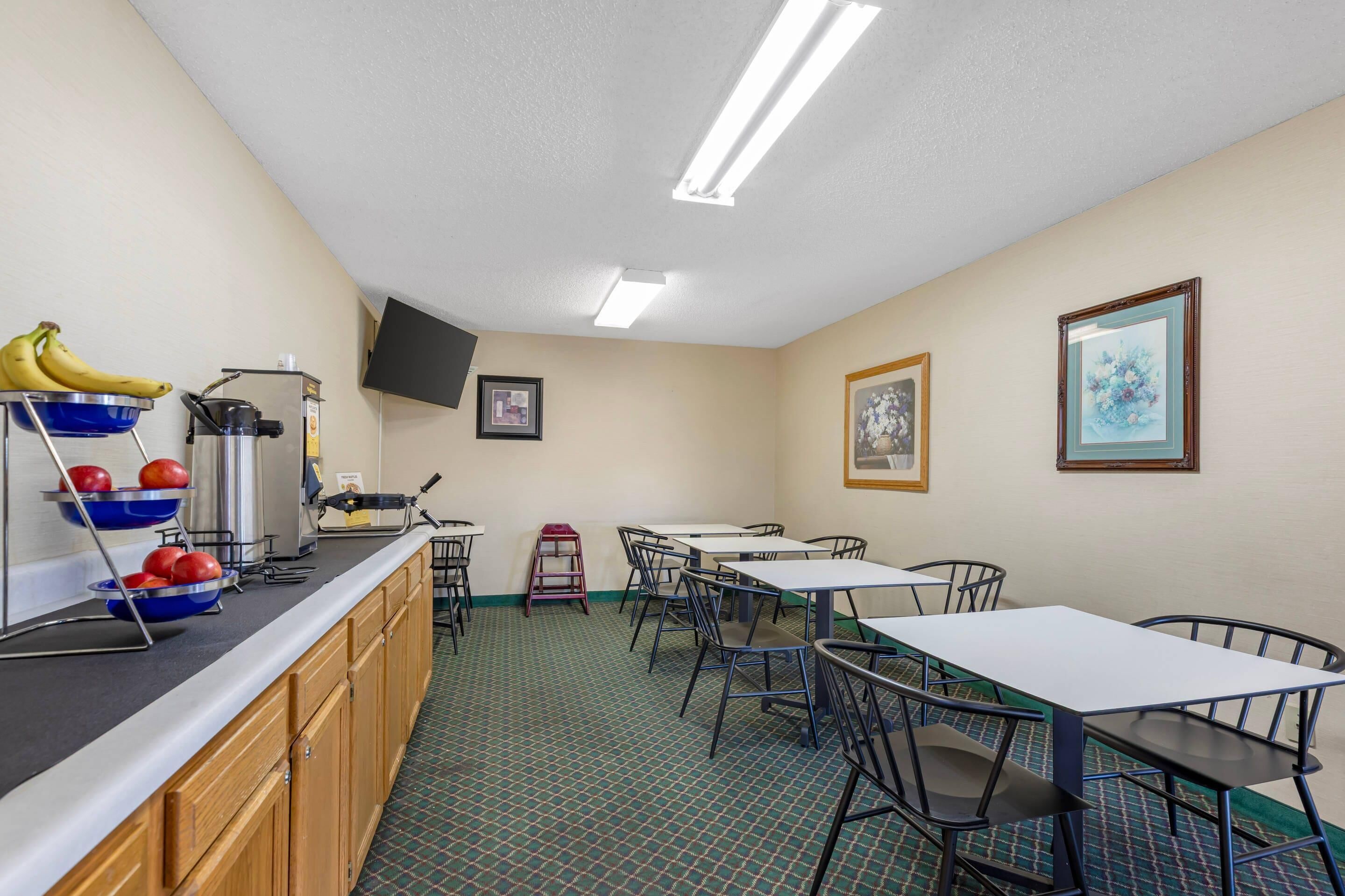 A dining area with tables and chairs, a counter with fruits, a coffee machine, and artwork on the walls.
