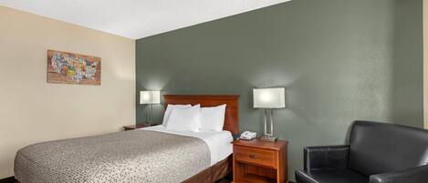 A hotel room with a bed, bedside tables, a chair, and a wall map.