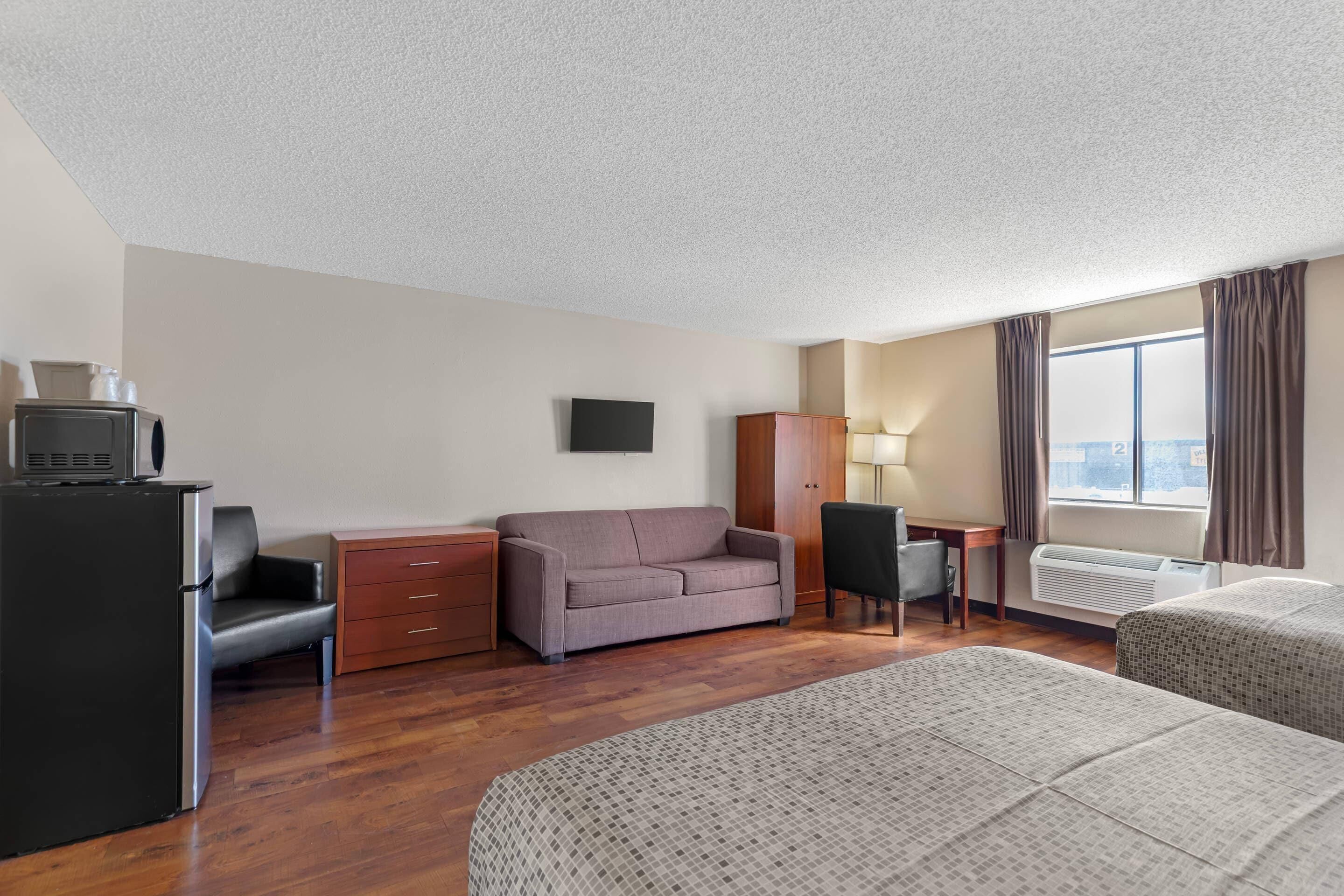 Een hotelkamer met een kitchenette, een bank, een bureau, een stoel en een bed.