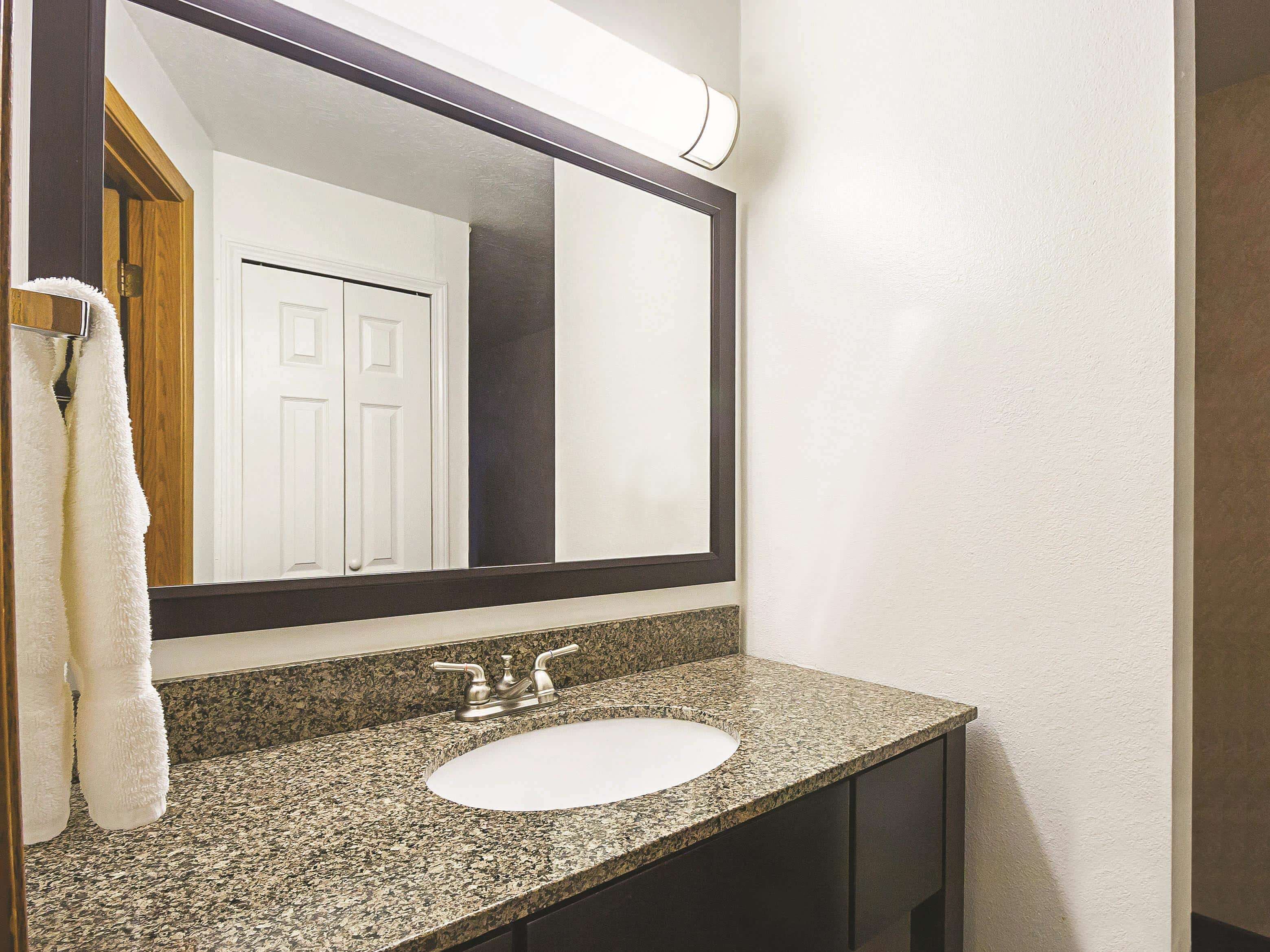Un baño con encimera de granito, lavamanos blanco y un espejo grande.
