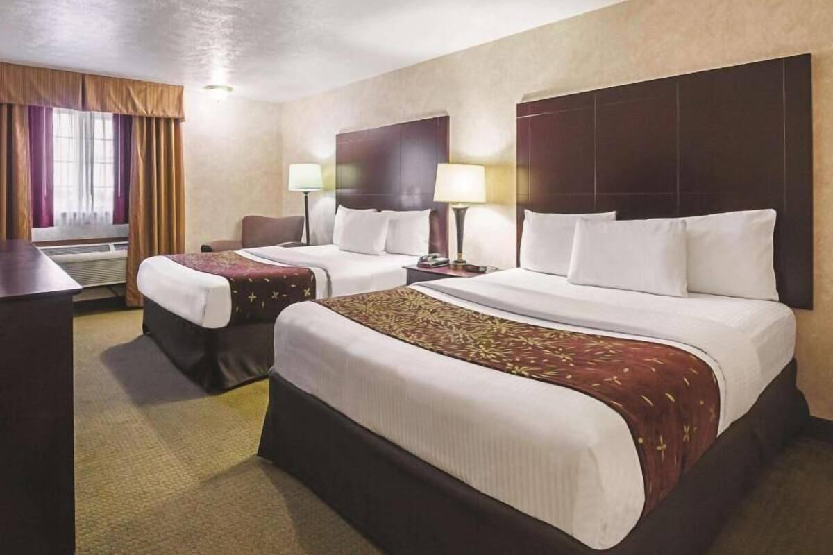 A hotel room with two beds, a desk, a chair, a lamp, and a window with curtains.