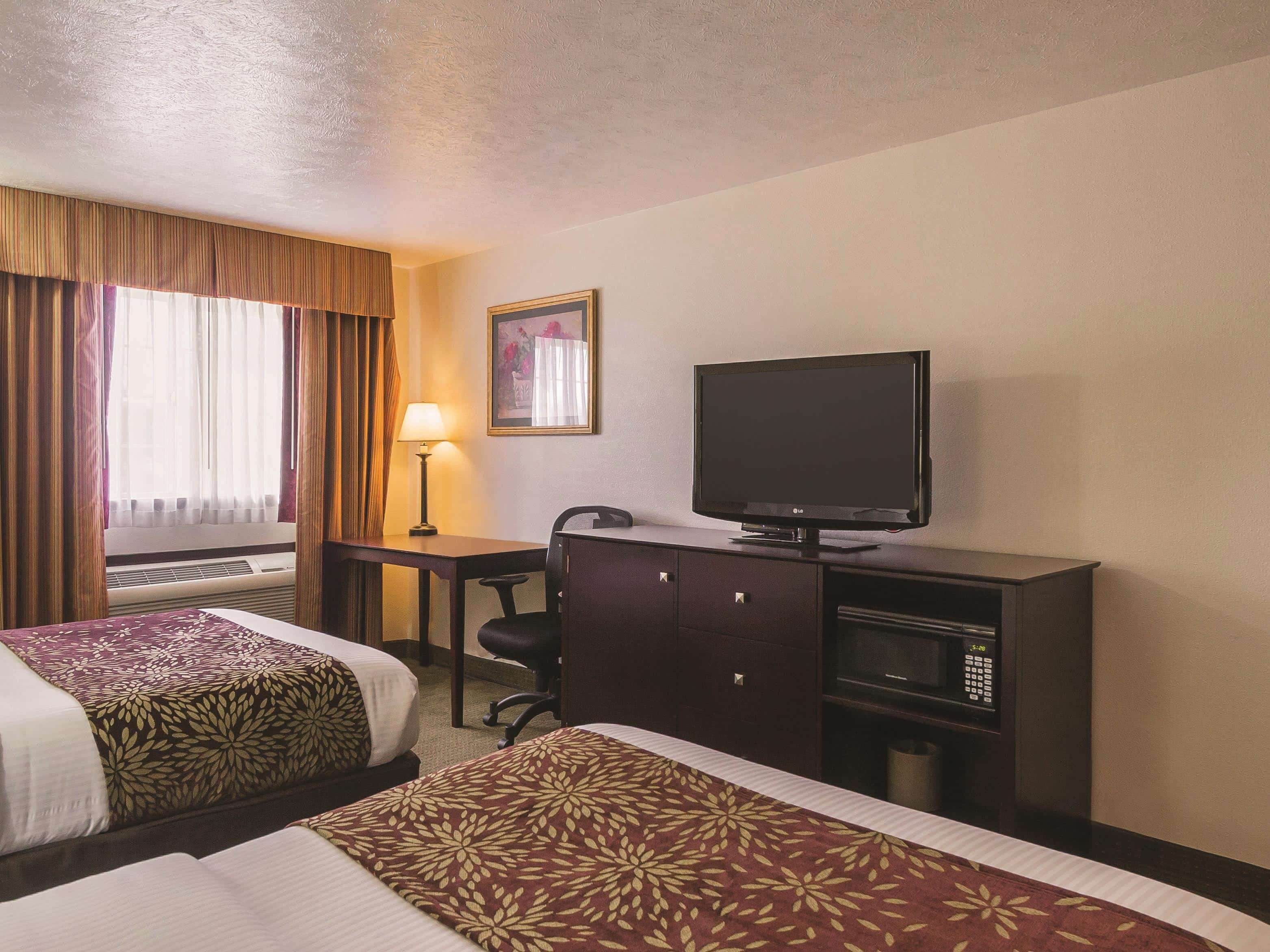 Una habitación de hotel con dos camas, un escritorio con lámpara, televisor y minibar.