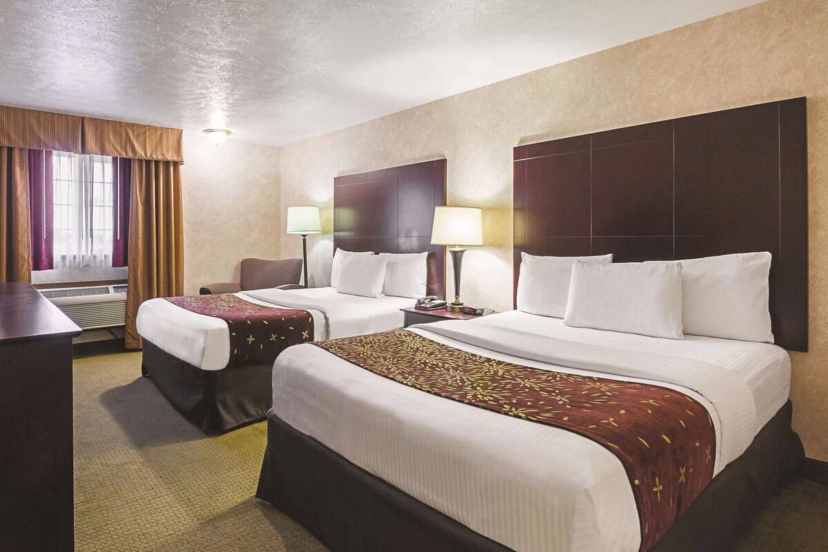 A hotel room with two beds, a desk, and a chair.