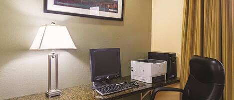 Un espacio de trabajo en un hotel, con escritorio, computadora, impresora y una silla.