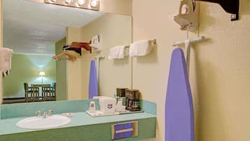 Ein Badezimmer mit Waschbecken, Spiegel, Handtuchhalter und einer Kaffeemaschine.