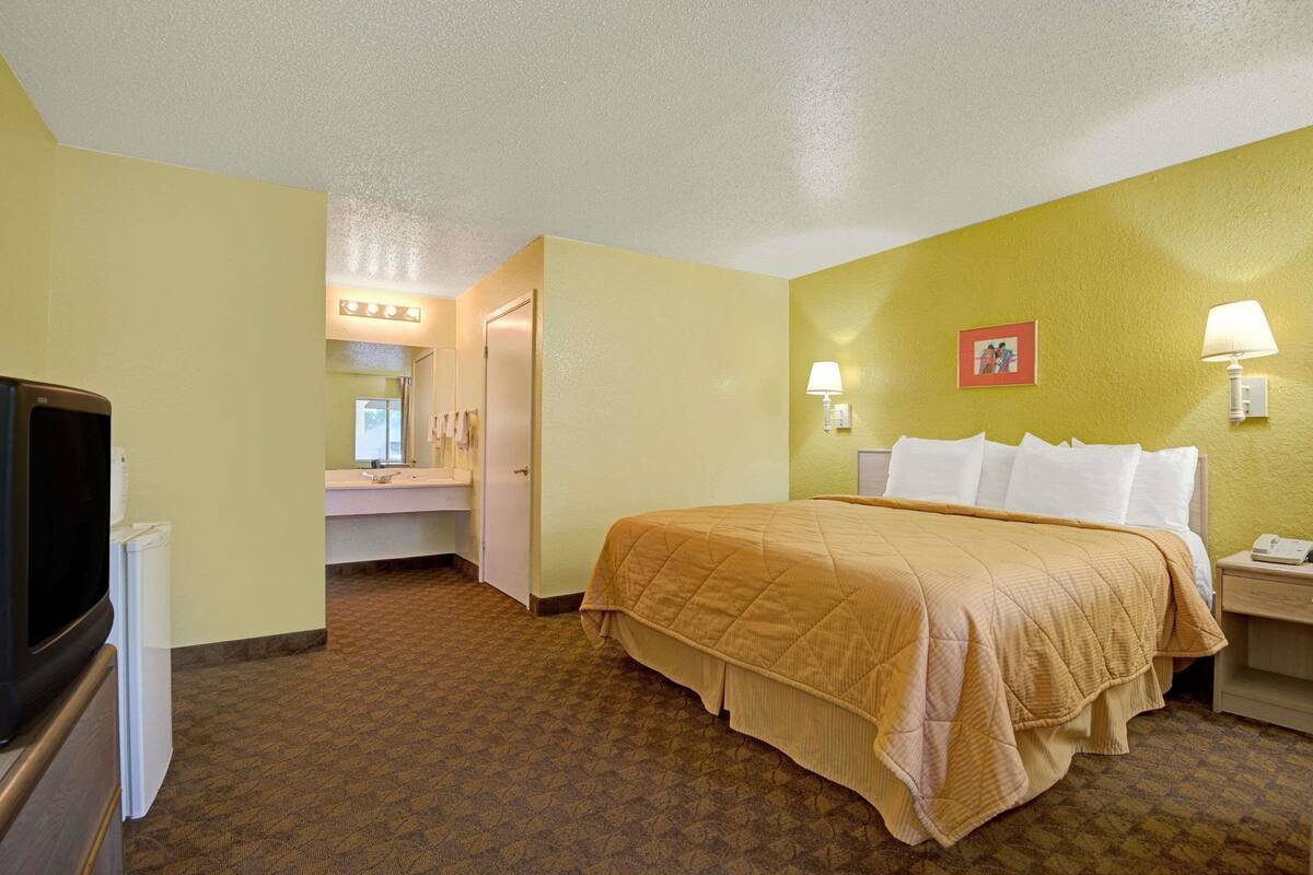 A hotel room with a bed, bedside lamps, a TV, and a bathroom with a mirror and lights.