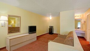 Hotelkamer met een bank, een televisie op een houten console, een magnetron en een badkamer met een spiegel en verlichting.