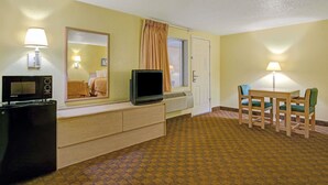 Een hotelkamer met een bed, een bureau met een computer, een televisie, een spiegel, een raam met gordijnen en een zithoek met stoelen en een tafel.