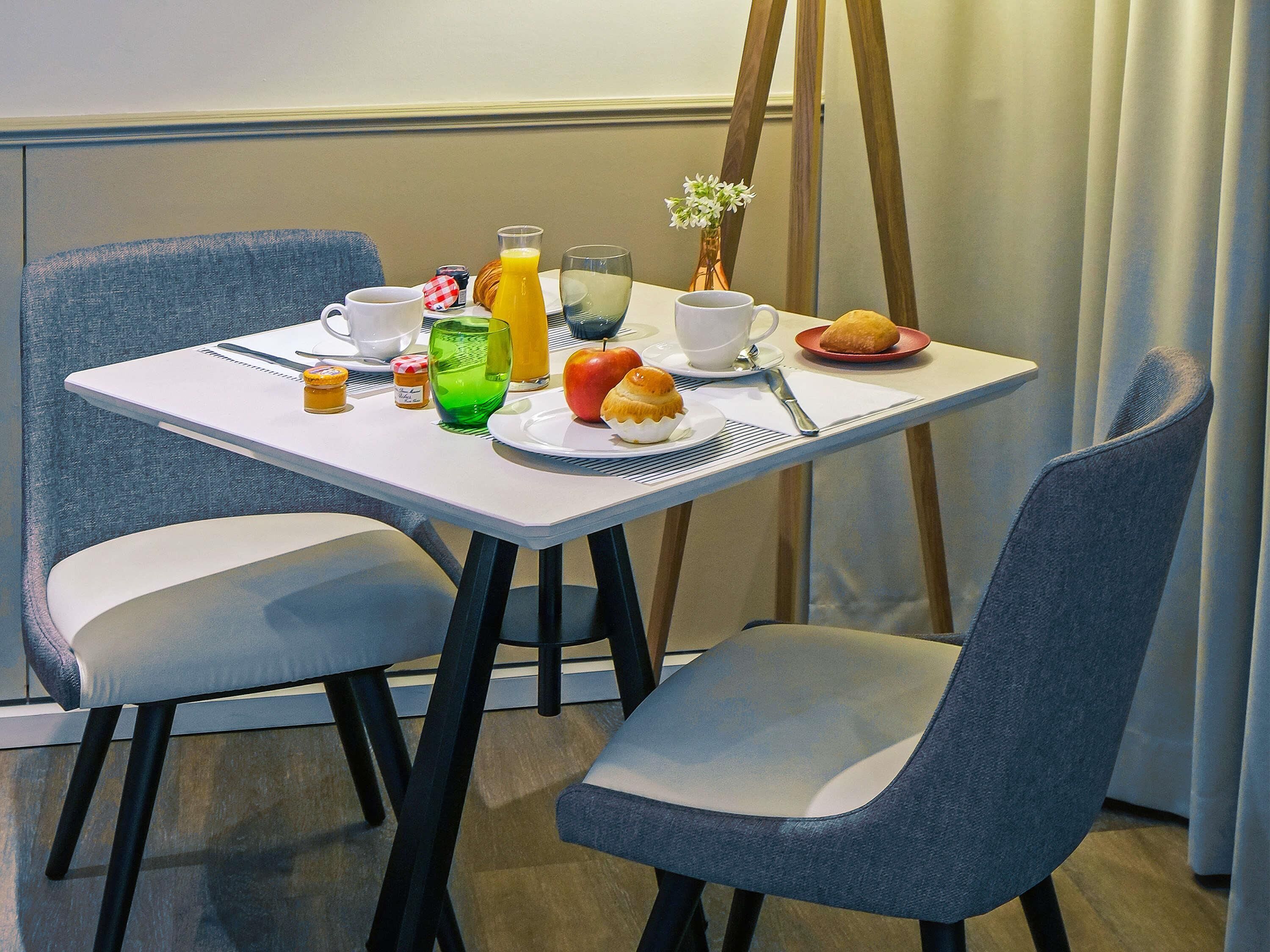 Ein Frühstückstisch mit Tasse, Glas, Apfel, Croissant und einer kleinen Vase mit Blumen.