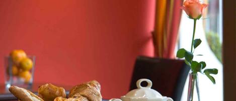Una mesa de desayuno con pastelería, fruta, un calentador de té, una taza y una rosa.