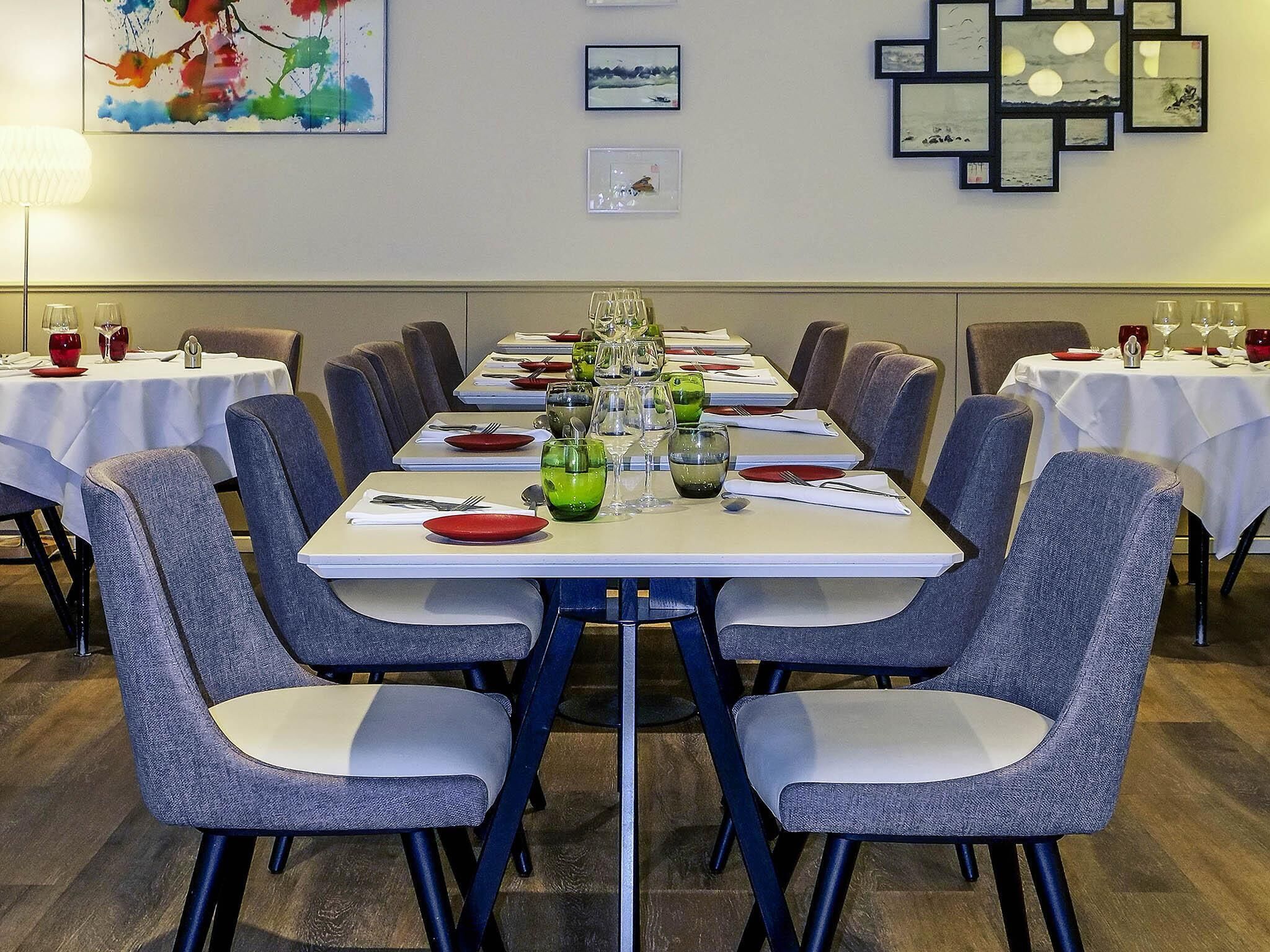 A dining area with tables set for a meal, chairs, and framed artwork on the walls.