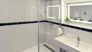 Un baño moderno con ducha envuelta en vidrio, lavamanos blanco y un espejo grande.