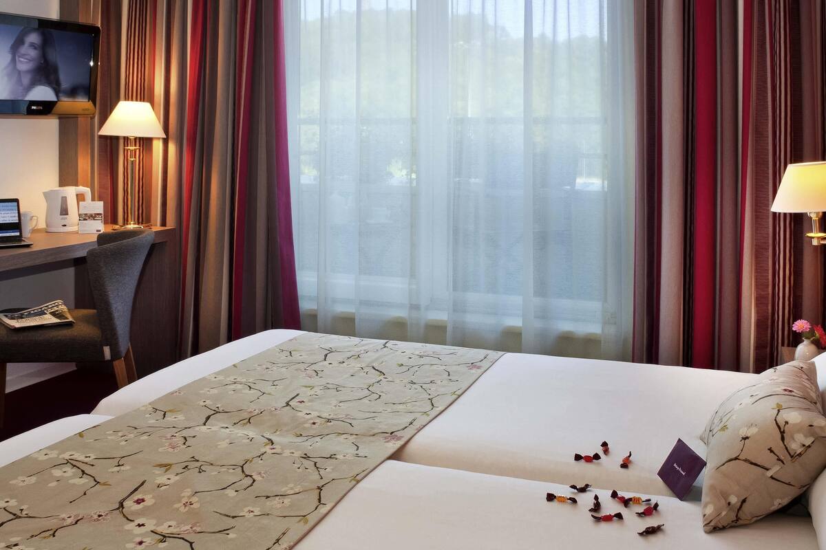A hotel room with a bed, a desk with a laptop, a television, and a window with curtains.