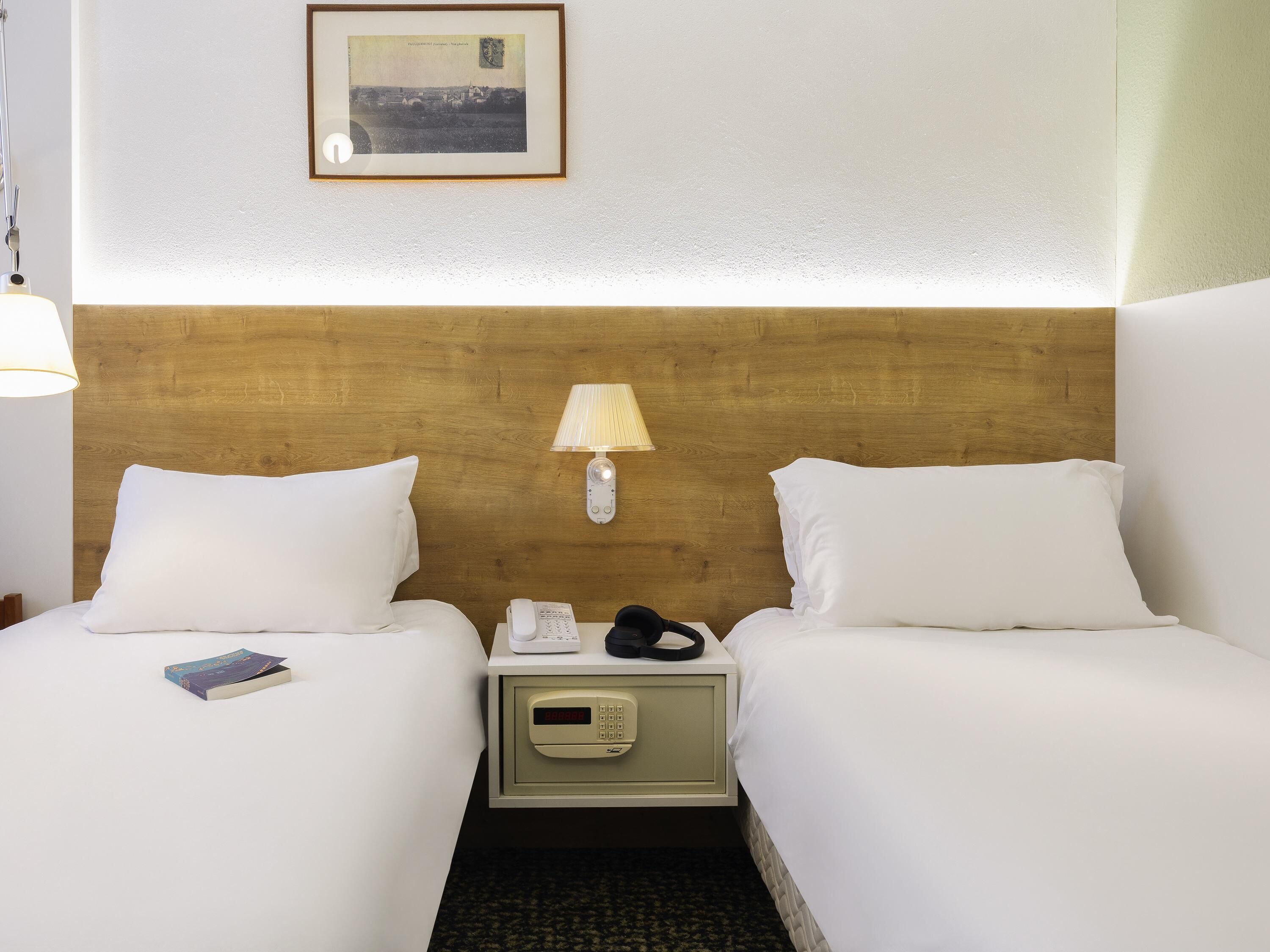 Habitación de hotel con dos camas, una mesita de noche con lámpara, teléfono y reloj digital.