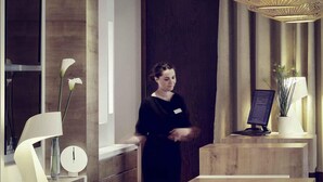 A hotel reception desk with a modern design, featuring a wooden counter, a computer, and a potted plant. - Mercure Forbach (Forbach)