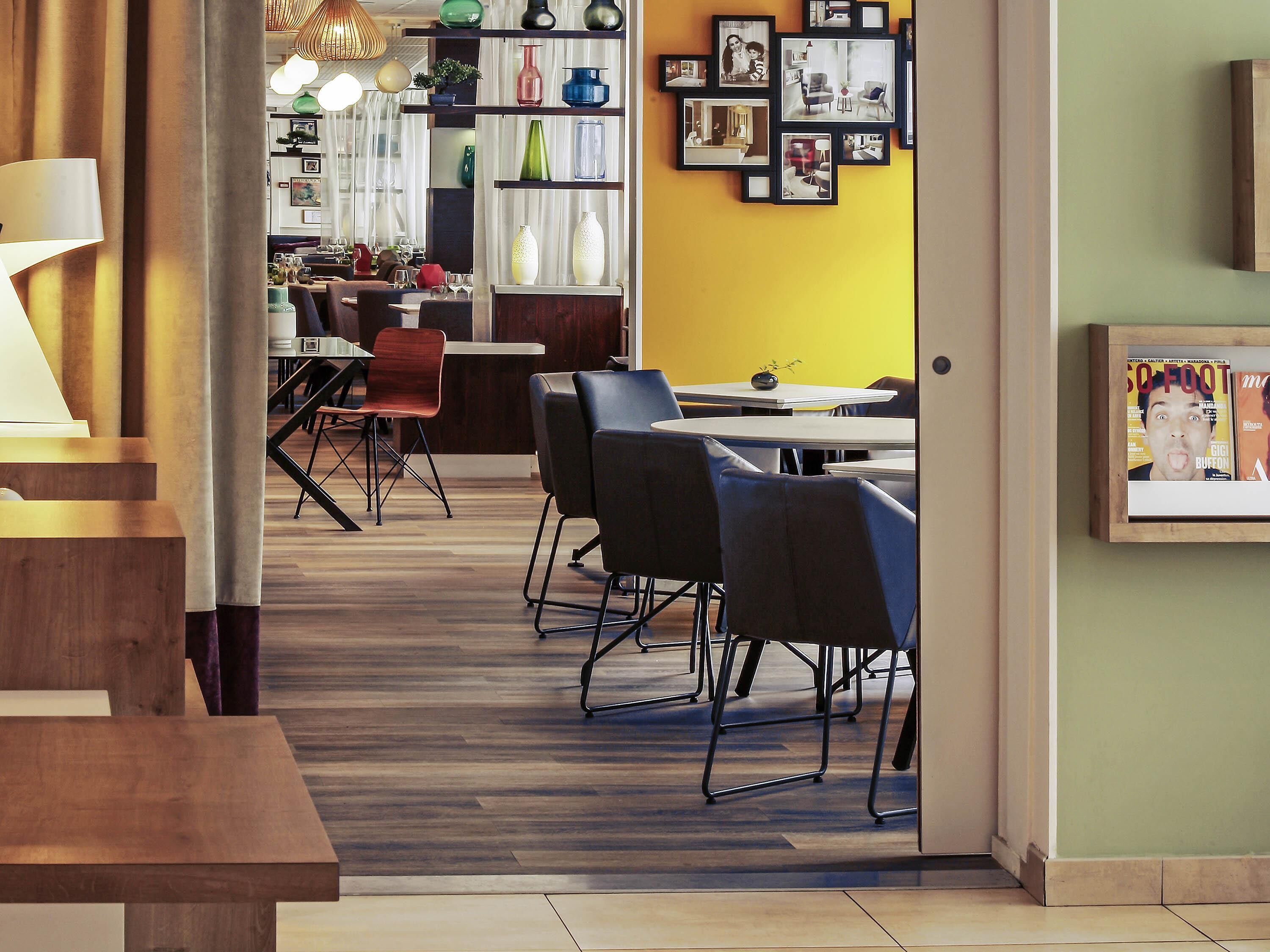 Un área de comedor moderna con suelo de madera, sillas negras y una pared de acento amarilla.