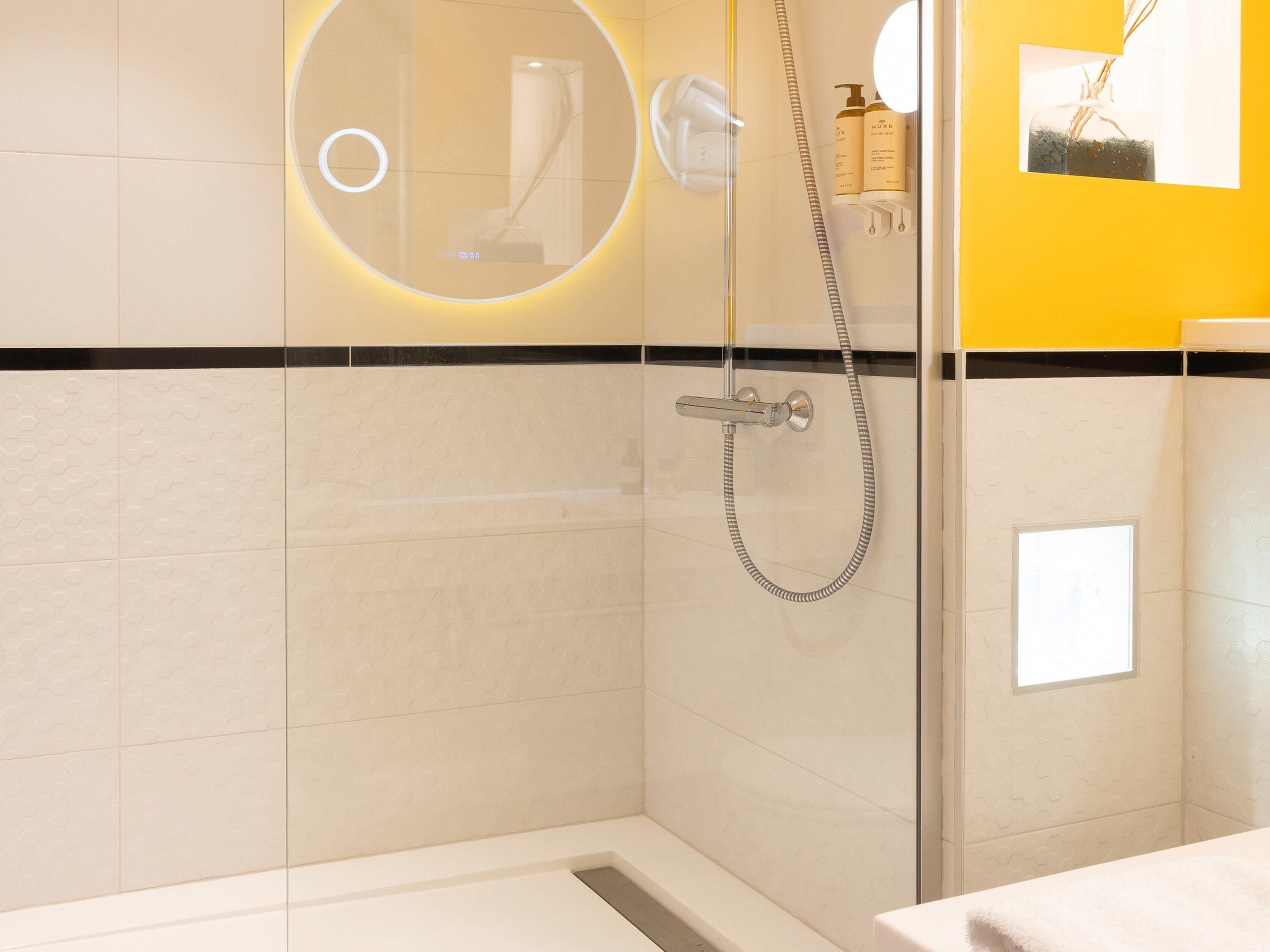 A modern bathroom with a glass-enclosed shower, a white sink, and a yellow accent wall.