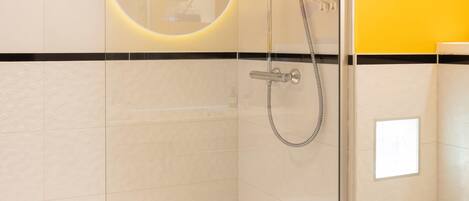 Un baño moderno con ducha envuelta en vidrio, un lavamanos blanco y una pared de acento amarilla.