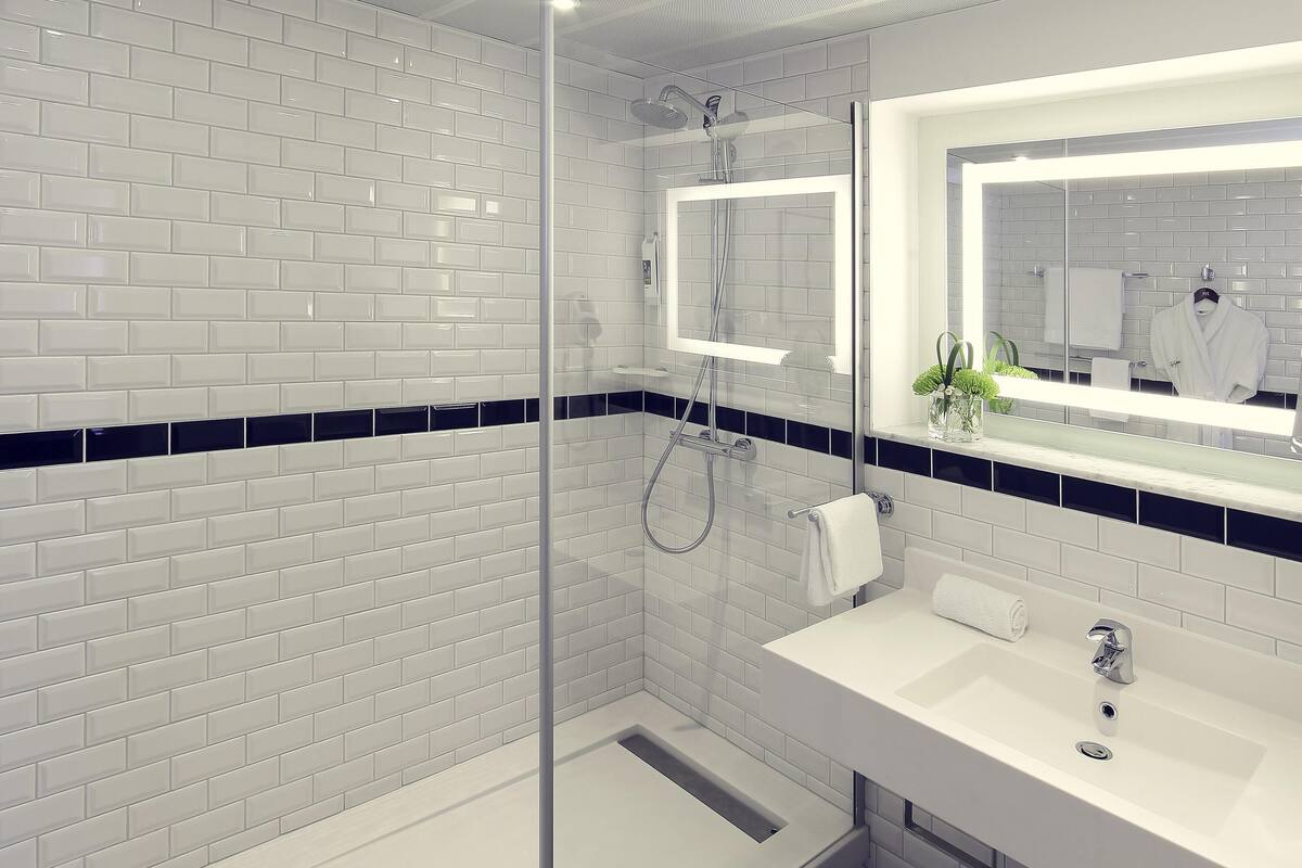A modern bathroom with white subway tiles, a glass shower enclosure, a white sink, and a mirror with a towel rack.