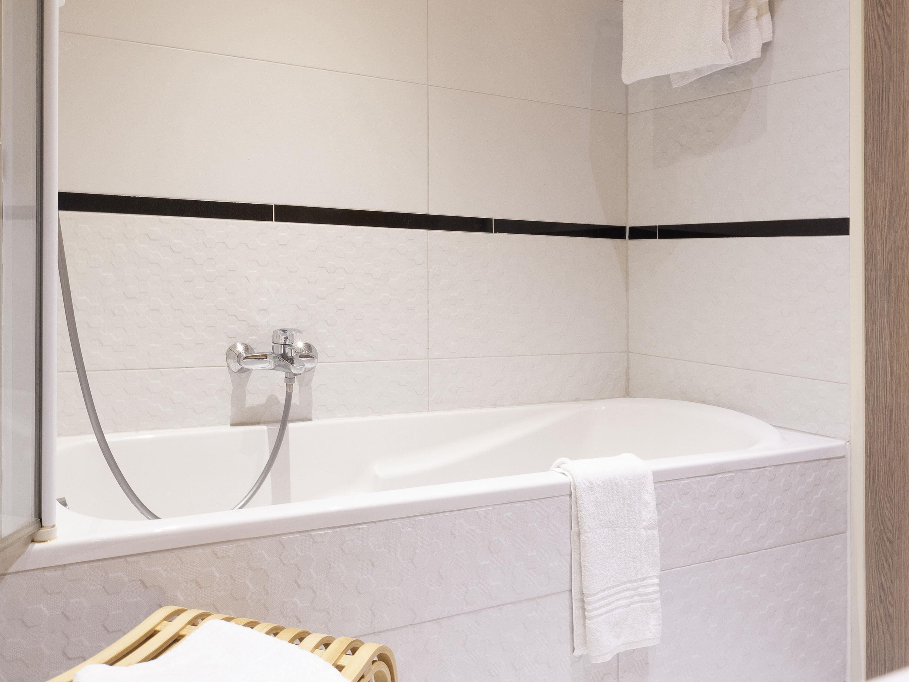 A modern bathroom with a bathtub, a shower, and a wooden stool.